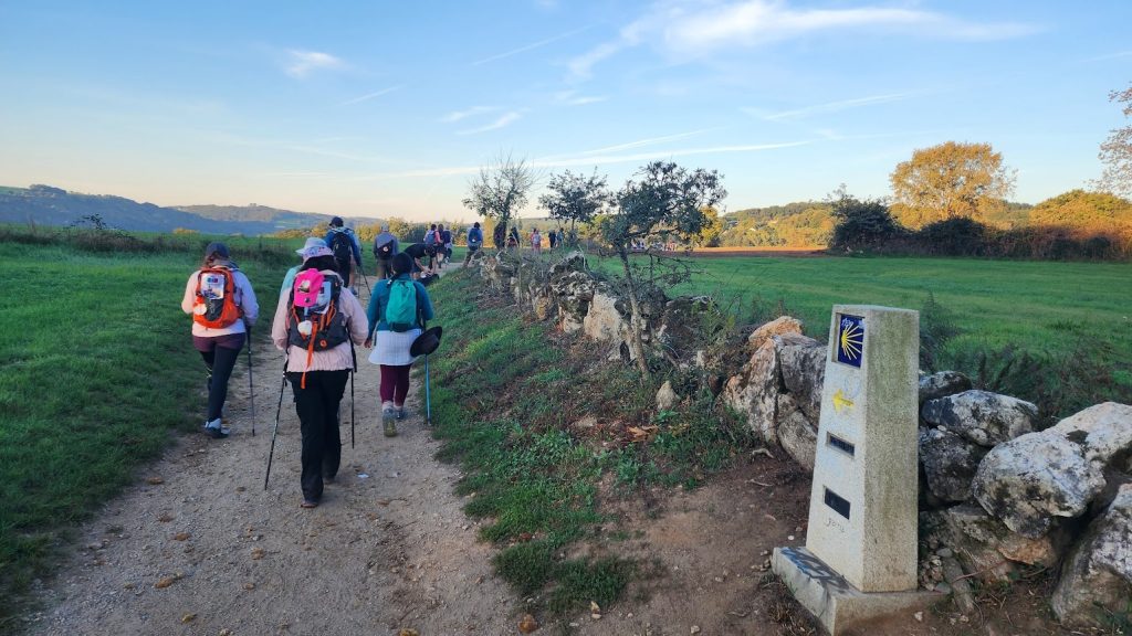 Peregrinos recorriendo el Camino de Santiago desde Sarria al amanecer, rodeados de naturaleza.