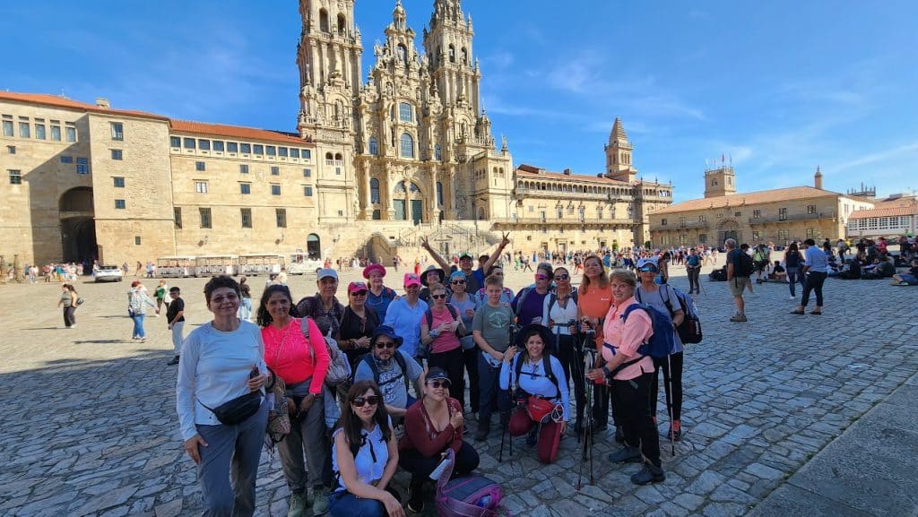 Peregrinos caminando por el Camino de Santiago con mochilas ligeras, disfrutando de un recorrido todo incluido, rodeados de paisajes verdes. camino de santiago todo incluido