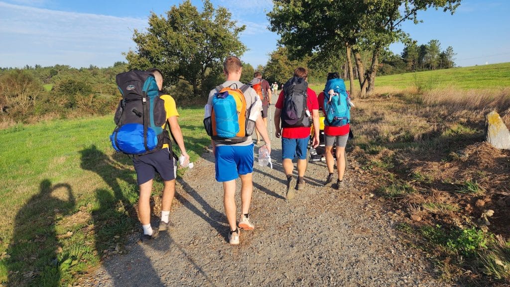 Peregrinos caminando por el Camino Primitivo desde Oviedo, rodeados de montañas y paisajes verdes hacia Santiago de Compostela.